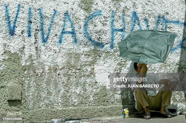 Resident, sitting in front of a graffiti reading: "LIVE CHAVEZ, in a street in downtown Caracas 23 October, 2002. Venezuela's military "utterly"...