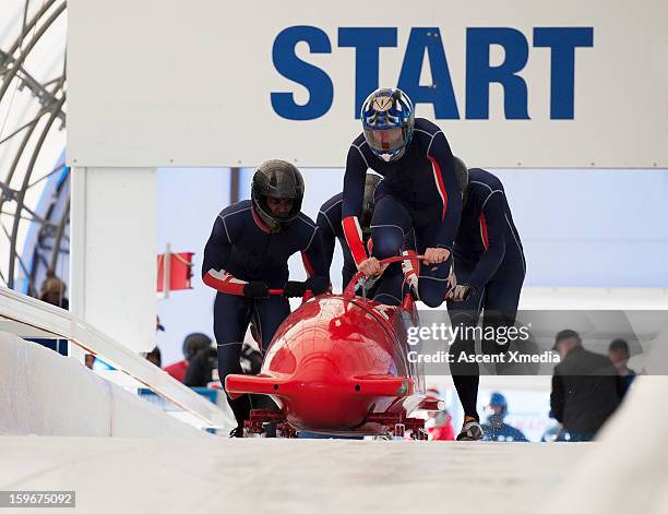 team of bobsledders push bobsled out of start gate - bob stock-fotos und bilder