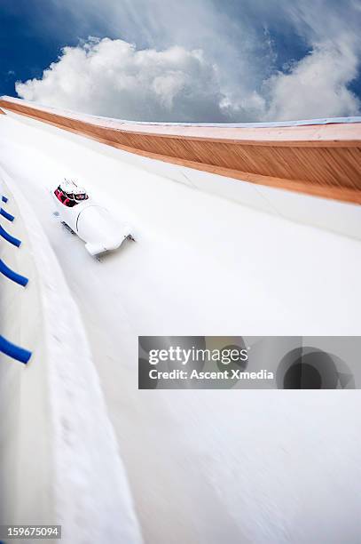 bobsled descends track with speed, clouds behind - bobsleigh stock pictures, royalty-free photos & images
