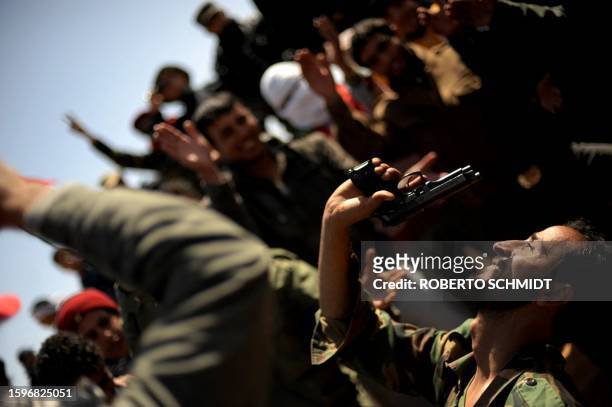Libyan rebel waves his hand gun as he gather with fellow fighters at a checkpoint in the outskirts of the key oil port of Ras Lanuf on March 7, 2011....