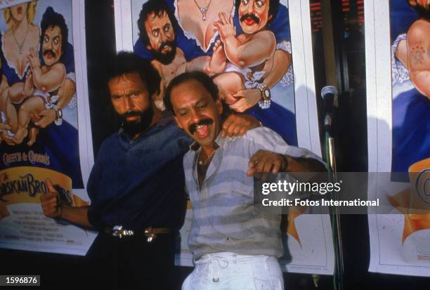 Comic actors Tommy Chong and Cheech Marin embrace in front of movie posters while promoting their film, 'Cheech and Chong's The Corsican Brothers,'...