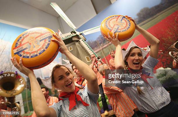 Young women promoting cheese from Holland hold up wheels of Dutch gouda as a brass band plays behind at the 2013 Gruene Woche agricultural trade fair...