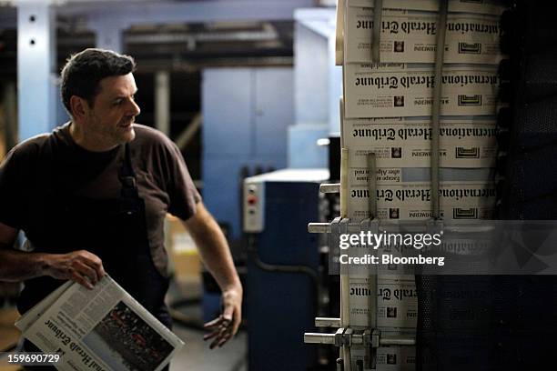 Worker inspects newly-printed editions of the International Herald Tribune newspaper at the Kathimerini printing plant in Paiania, Greece, on...