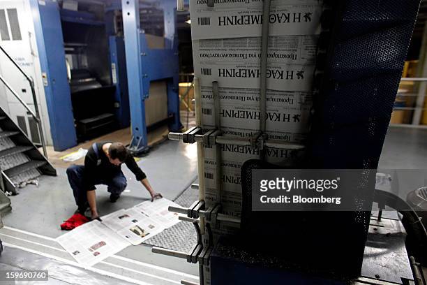 Worker inspects a newly-printed edition of the Kathimerini newspaper near the automated production line at the Kathimerini printing plant in Paiania,...