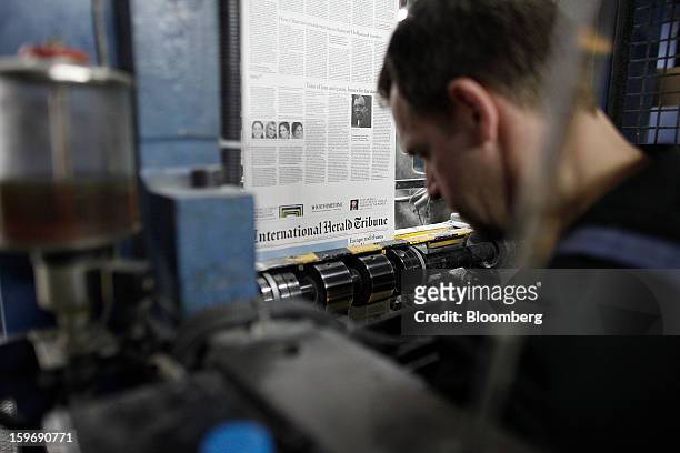 Worker watches as pages of the International Herald Tribune newpaper run through the print presses at the Kathimerini printing plant in Paiania,...
