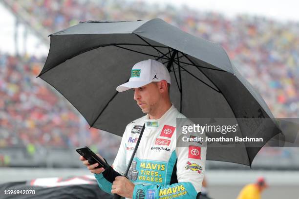 Denny Hamlin, driver of the Mavis Tires & Brakes Toyota, waits on the grid under an umbrella during a weather delay of the NASCAR Cup Series...