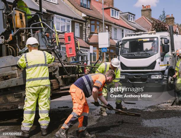 construction worker laying down tarmac - lavori stradali foto e immagini stock