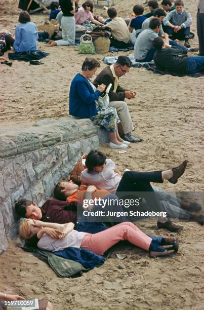 Young couples huddle together at the beach in Britain, circa 1965.