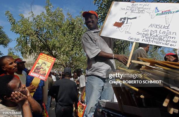 An opponent of Haitian President Jean Bertrand Aristide displays a poster 15 February 2004 in Port-au-Prince, showing Aristide attempting to flee the...