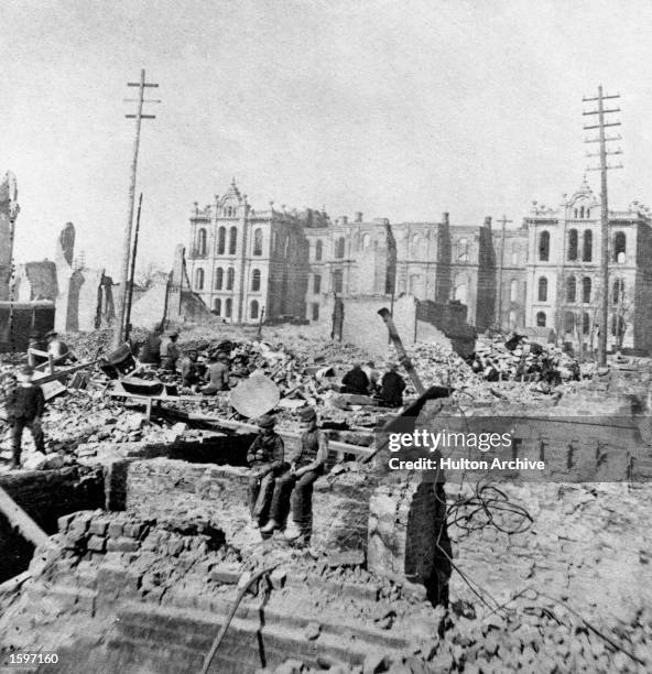 Two boys sit on top of a partial stone wall in the wreckage of a burned-out building at Madison and Clark Streets, with the Court House in the...