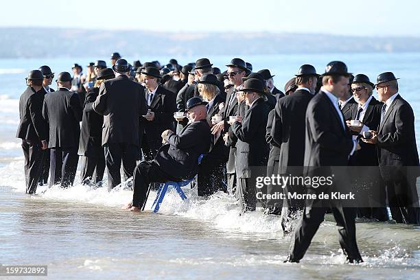 Participants stand on the beach dressed in suits and bowler hats as part of an art installation created by surrealist artist Andrew Baines on January...