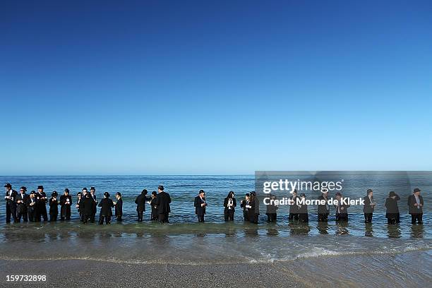 Participants stand on the beach dressed in suits and bowler hats as part of an art installation created by surrealist artist Andrew Baines on January...