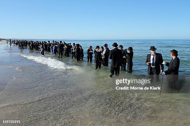 Participants stand on the beach dressed in suits and bowler hats as part of an art installation created by surrealist artist Andrew Baines on January...