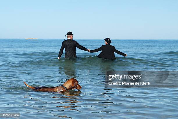 Dog swims by as participants stand in the water while wearing suits and bowler hats as part of an art installation created by surrealist artist...