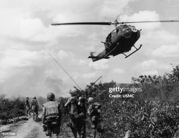 Soldiers of the fourth U.S. Marine Regiment patrol the demilitarized zone in Vietnam as a Marine Corps "Huey" helicopter passes overhead, Vietnam...