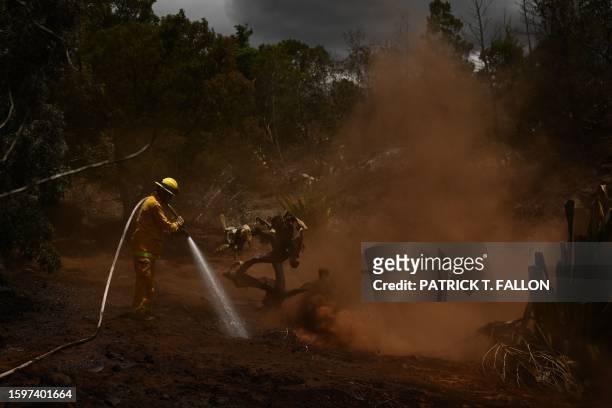 Maui County firefighter uses a hose line to extinguish a fire near homes during the upcountry Maui wildfires in Kula, Hawaii on August 13, 2023. The...