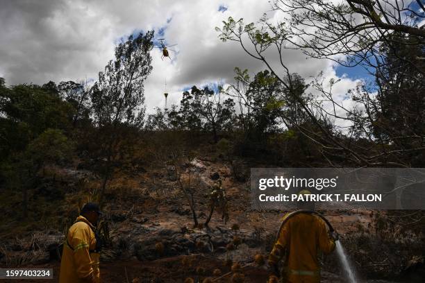 Firefighting helicopter makes a water drop as a Maui County firefighter extinguishes a fire near homes during the upcountry Maui wildfires in Kula,...