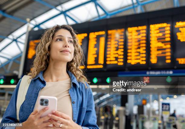 woman at the train station checking the departure board and using her phone - london train stock pictures, royalty-free photos & images
