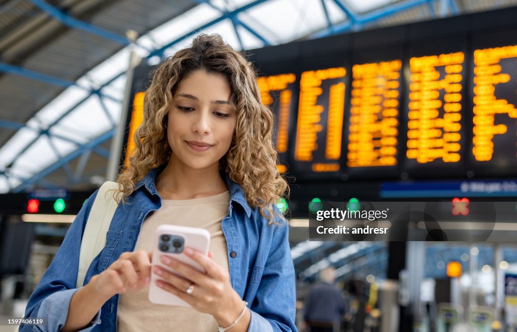 Woman at the train station using her phone while checking the departure board