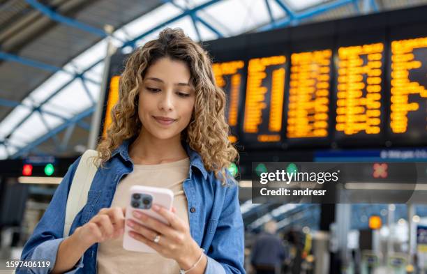 woman at the train station using her phone while checking the departure board - aeroplane ticket stock pictures, royalty-free photos & images