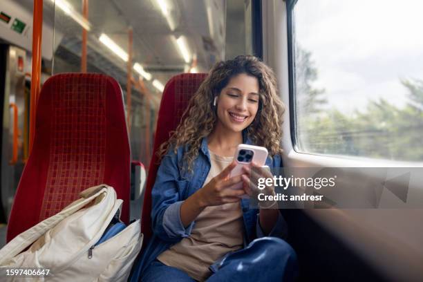 happy woman commuting on a train and checking her cell phone - wonen stock pictures, royalty-free photos & images