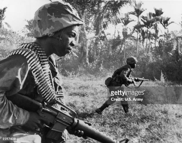 Riflemen from the 173rd Airborne Brigade charge toward Viet Cong positions, holding machine guns in a wooded area of War Zone D during the Vietnam...