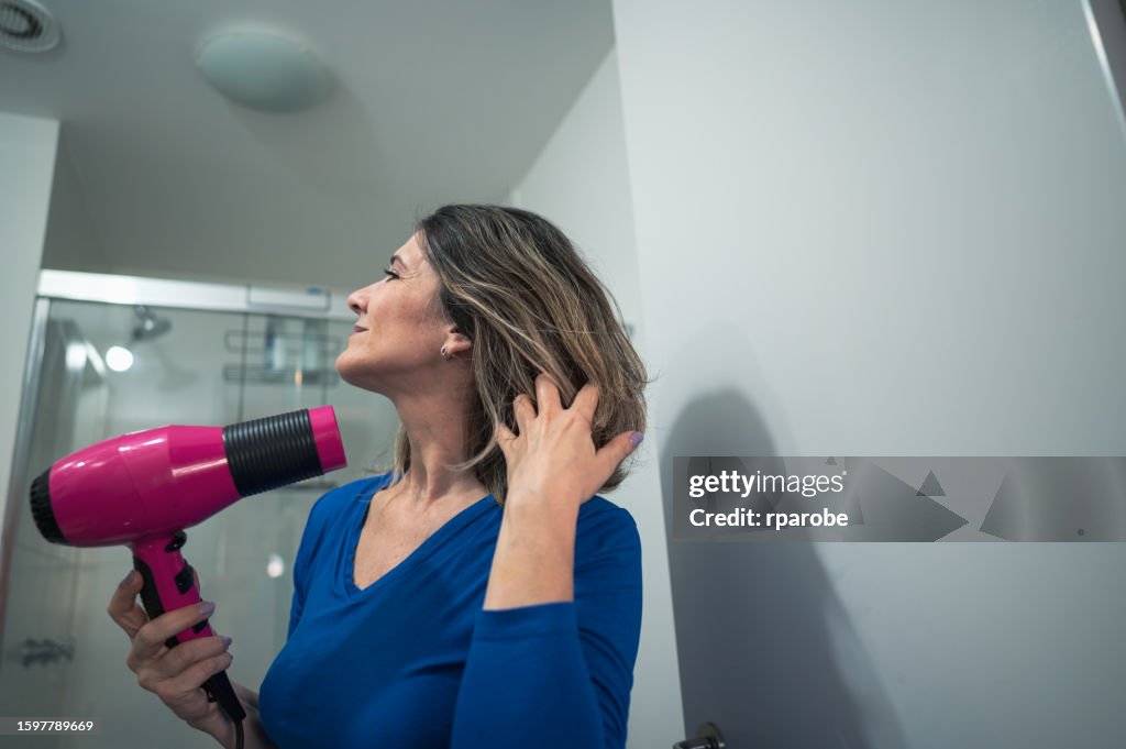 Uma mulher que usa eletricidade em casa para secar o cabelo com um secador elétrico