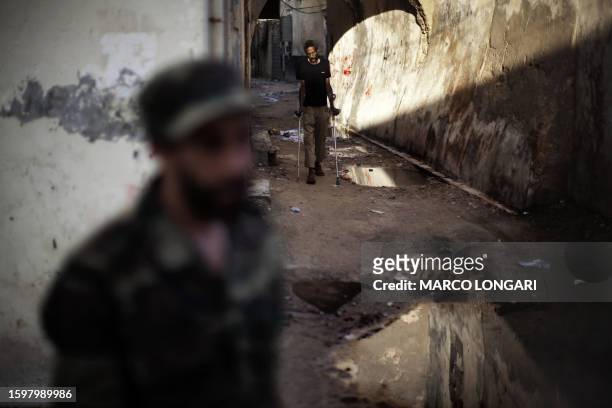 An immigrant walks on crutches in the "medina", or old Arab quarter, of Tripoli on October 4, 2011 as a National Transitional Council fighter patrols...