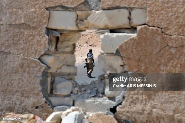 National Transitional Council fighter is seen through a hole in a wall at a checkpoint near Sirte on September 24, 2011. Fighters for Libya's interim...