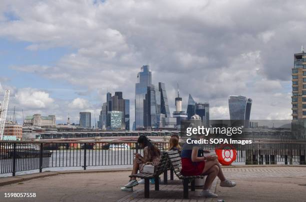 People relax in South Bank with a view of the City of London skyline on a partly cloudy day.