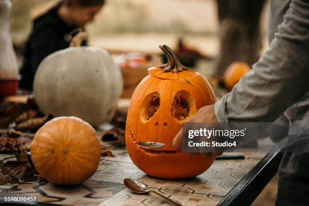 family celebrating halloween at home and preparing pumpkins. creative girl making a halloween decoration. - carve out stock pictures, royalty-free photos & images