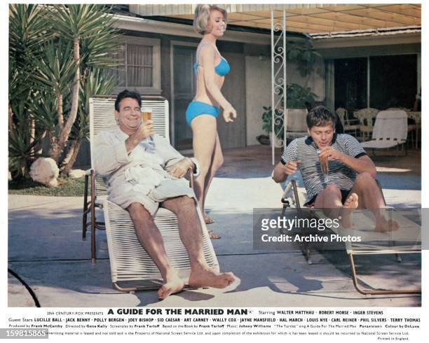 Inger Stevens walking by in a bikini, behind two men drinking a beer, seated in lounge chairs in a scene from the film 'A Guide For The Married Man',...