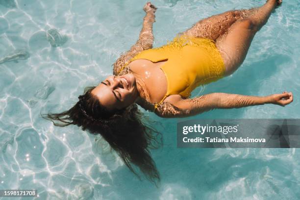 beautiful woman in yellow swimsuit lies on transparent sea water on a summer sunny day. - transparent-swimsuit stock pictures, royalty-free photos & images