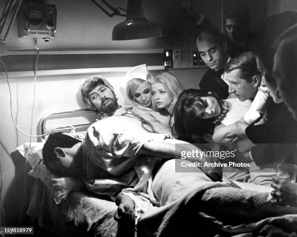 James Coburn, Ewa Aulin and others crowd on and around a hospital bed in a scene from the film 'Candy', 1968.