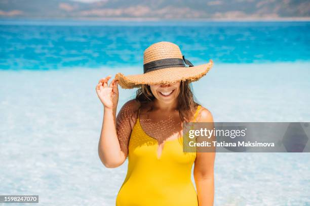 a woman in a yellow swimsuit and straw hat emerges from the sea with clear turquoise water on a summer sunny day. - women in bathing suits stock pictures, royalty-free photos & images