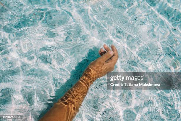 a woman's hand under clear water, beautiful sun glare on the skin. - swimming pool and hand stock-fotos und bilder