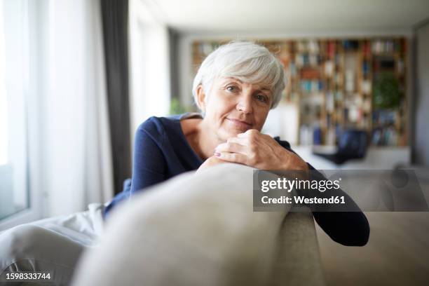 contemplating senior woman relaxing while sitting on sofa - tiefenschärfe stock-fotos und bilder