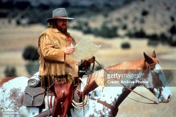 John Candy reads a map in a scene from the film 'Wagons East', 1994.