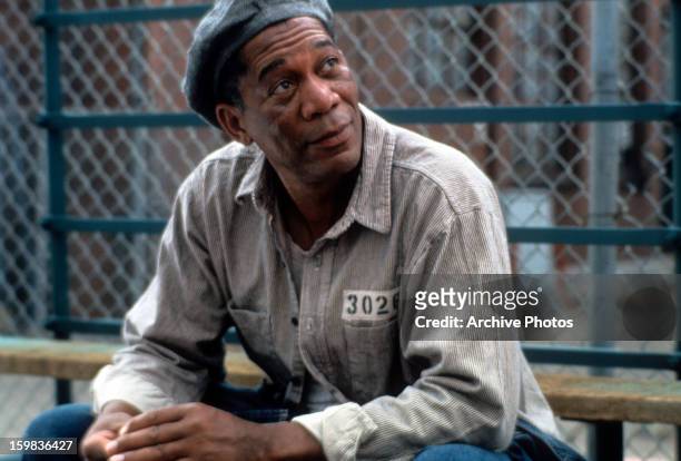 Morgan Freeman sitting outside with a hat and prison uniform on in a scene from the film 'The Shawshank Redemption', 1994.