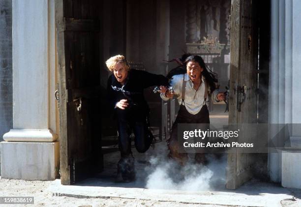 Owen Wilson and Jackie Chan barreling out of a building likes it's going to explode in a scene from the film 'Shanghai Noon', 2000.