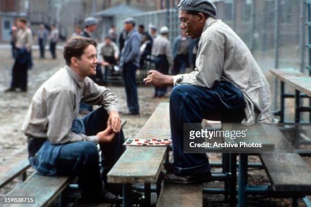 Tim Robbins and Morgan Freeman sitting outside on the benches playing checkers and talking in a scene from the film 'The Shawshank Redemption', 1994.