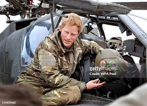 In this image released on January 21 Prince Harry, shows a television crew his flight helmet as he makes early morning checks as he sits on an Apache...
