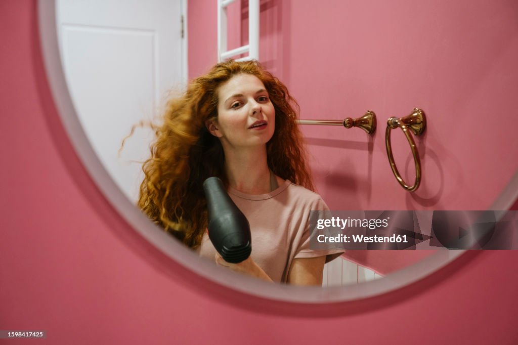 Woman drying hair looking in mirror at home