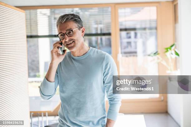 smiling businessman talking on smart phone in office - bien vestido fotografías e imágenes de stock