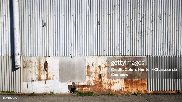corrugated metal plate wall painted and weathered white with rust, a tube and an asphalt street in montreal, quebec, canada - corrugated photos et images de collection