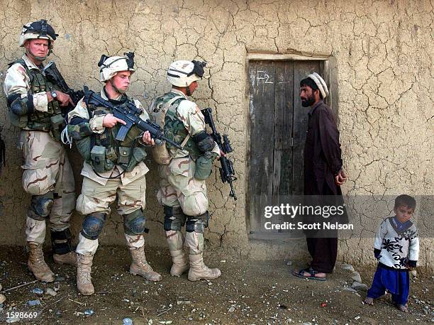 An Afghan man and his son watch as soldiers from the U.S. Army 82nd Airborne Division prepare to sweep their home November 7, 2002 in southeastern...