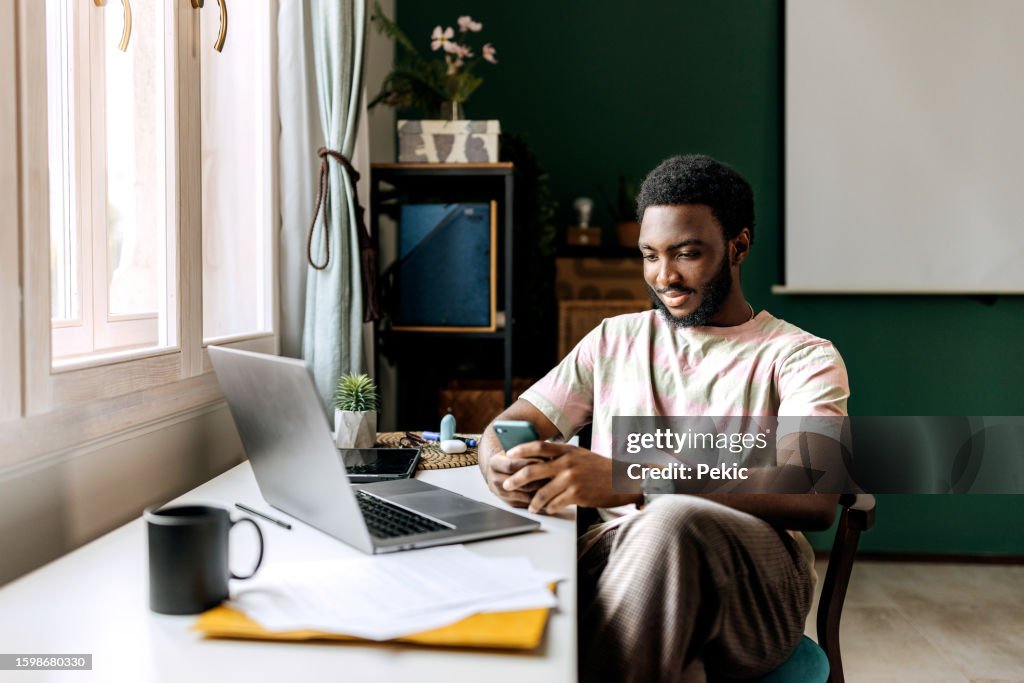 Young casually clothed man text messaging while working at home office