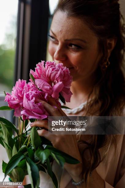 woman enjoying the smell of a beautiful bouquet of pink peonies by the window - close up of flower bouquet stock pictures, royalty-free photos & images