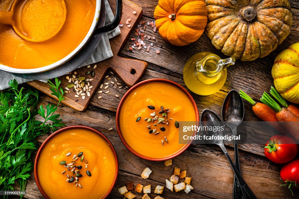 Deux bols de soupe à la citrouille pour le repas de Thanksgiving avec des ingrédients sur une table en bois rustique