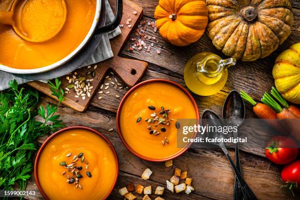 two bowls of pumpkin soup for thanksgiving meal with ingredients on rustic wooden table - root vegetables stock pictures, royalty-free photos & images